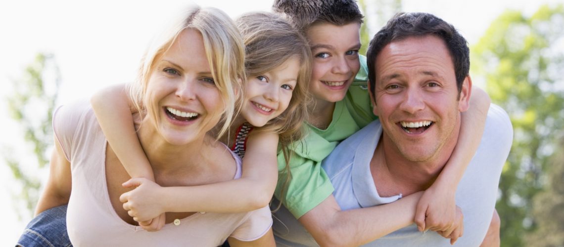 Couple giving two young children piggyback rides smiling
